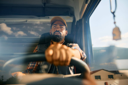 A truck driver is driving his truck. He is looking tired but determined.